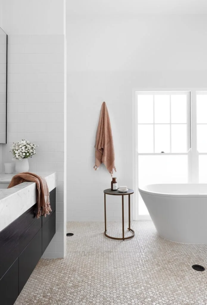 A classic white bathroom with a freestanding tub and black and white vanity.