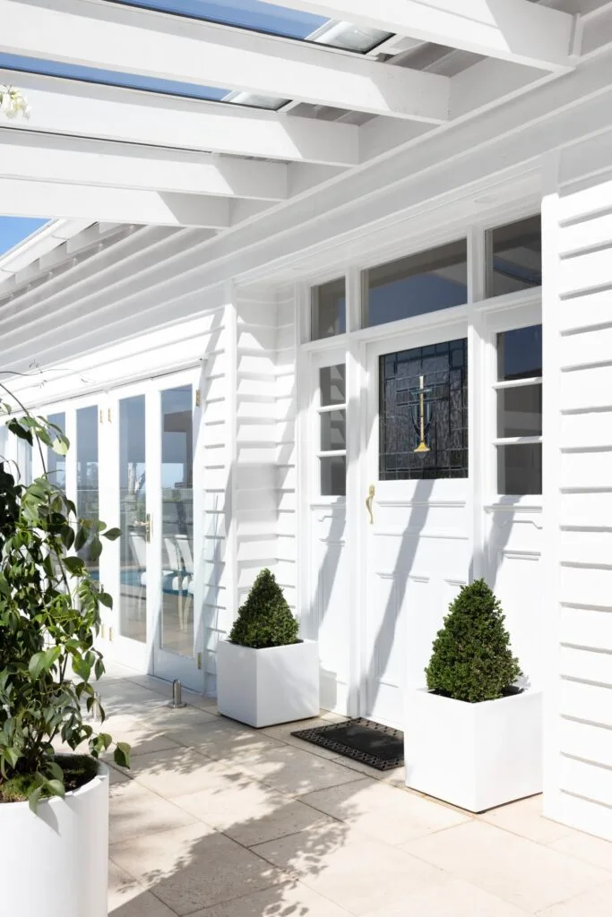 The white cladded bungalow entrance with a stained glass door.