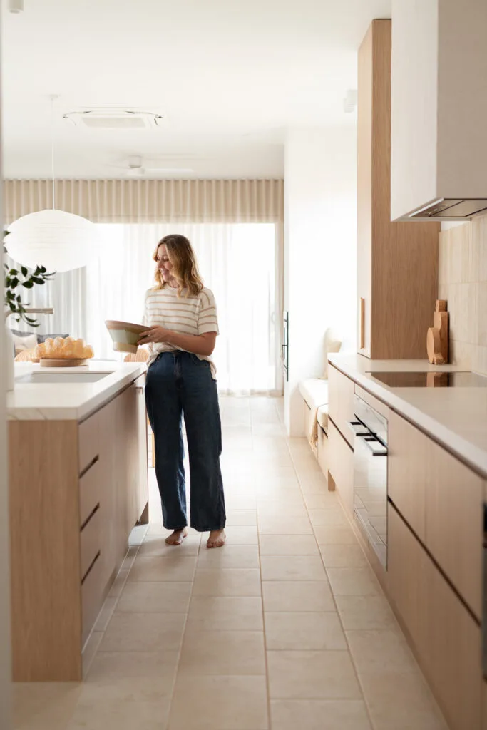 Jenna Densten standing in her modern farmhouse kitchen featuring a timber, neutral and soft green colour palette.