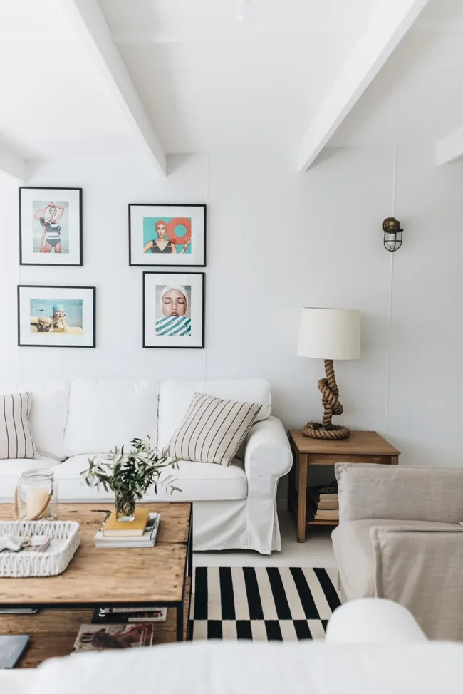 Cozy living room with white sofa, striped pillows, gallery wall art, rope lamp, and wooden coffee table.