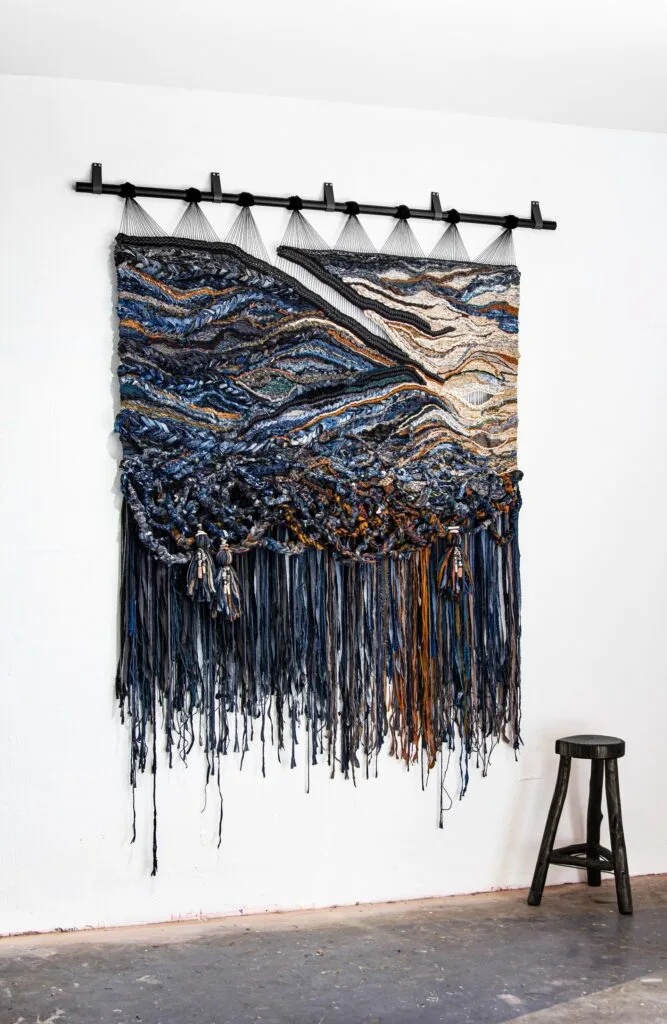 An abstract woven artwork hanging in a studio.