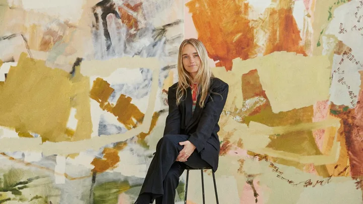 Australian artist Ash Holmes sitting in her studio before large orange abstract paintings.
