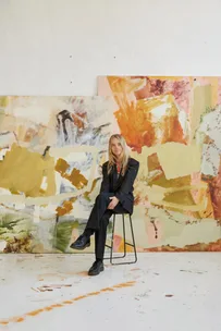 Australian artist Ash Holmes sitting in her studio before large orange abstract paintings.