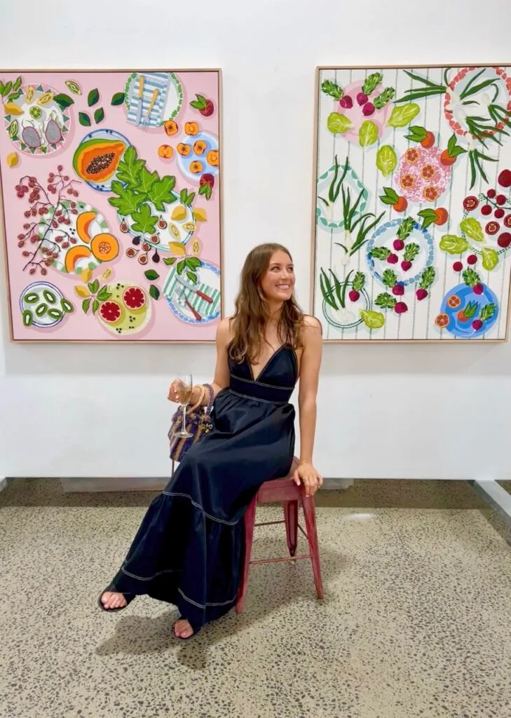 Australian artist Emma Sheehan sitting by two bright fruit artworks.