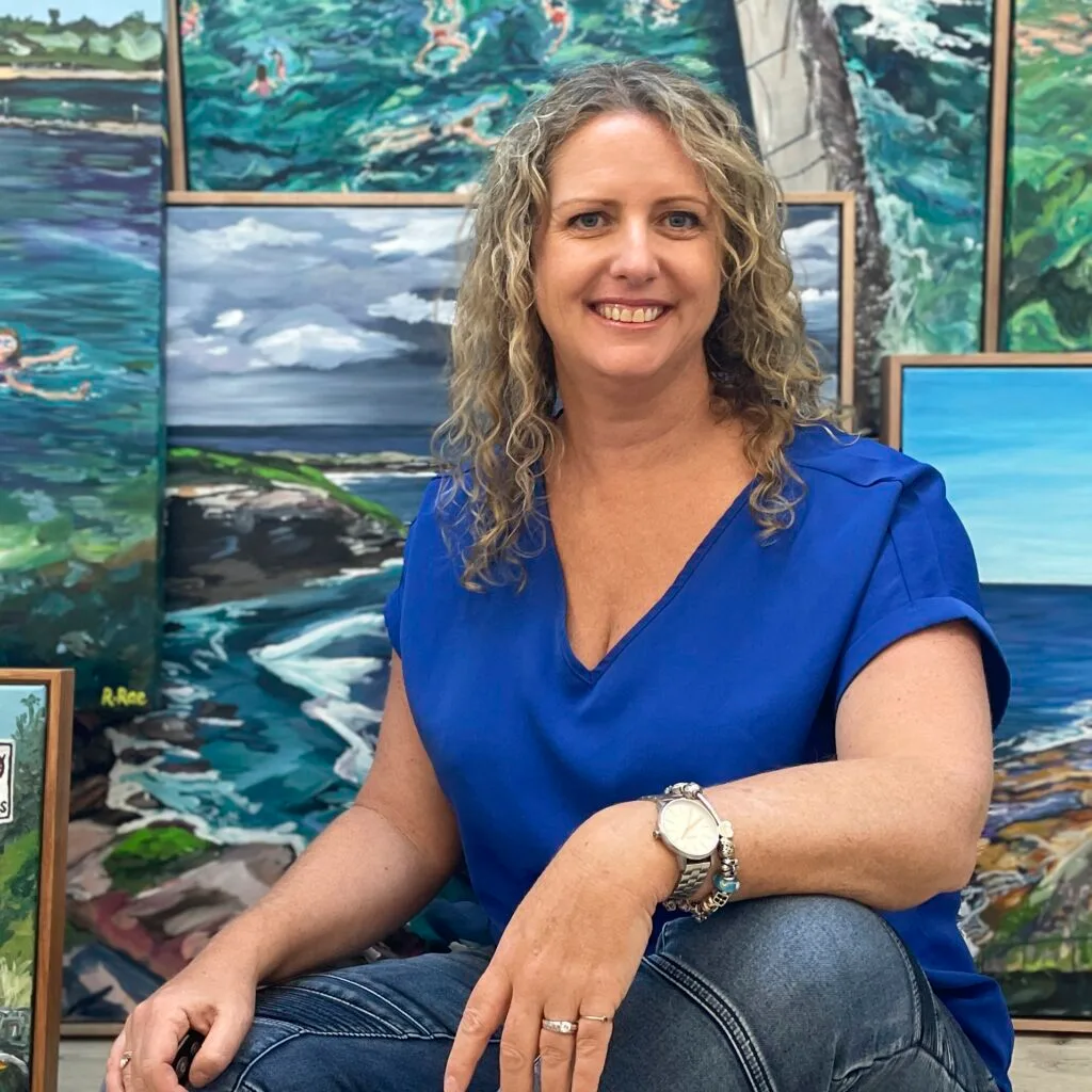 Australian artist Rachel Rae sitting by a collection of ocean artworks.