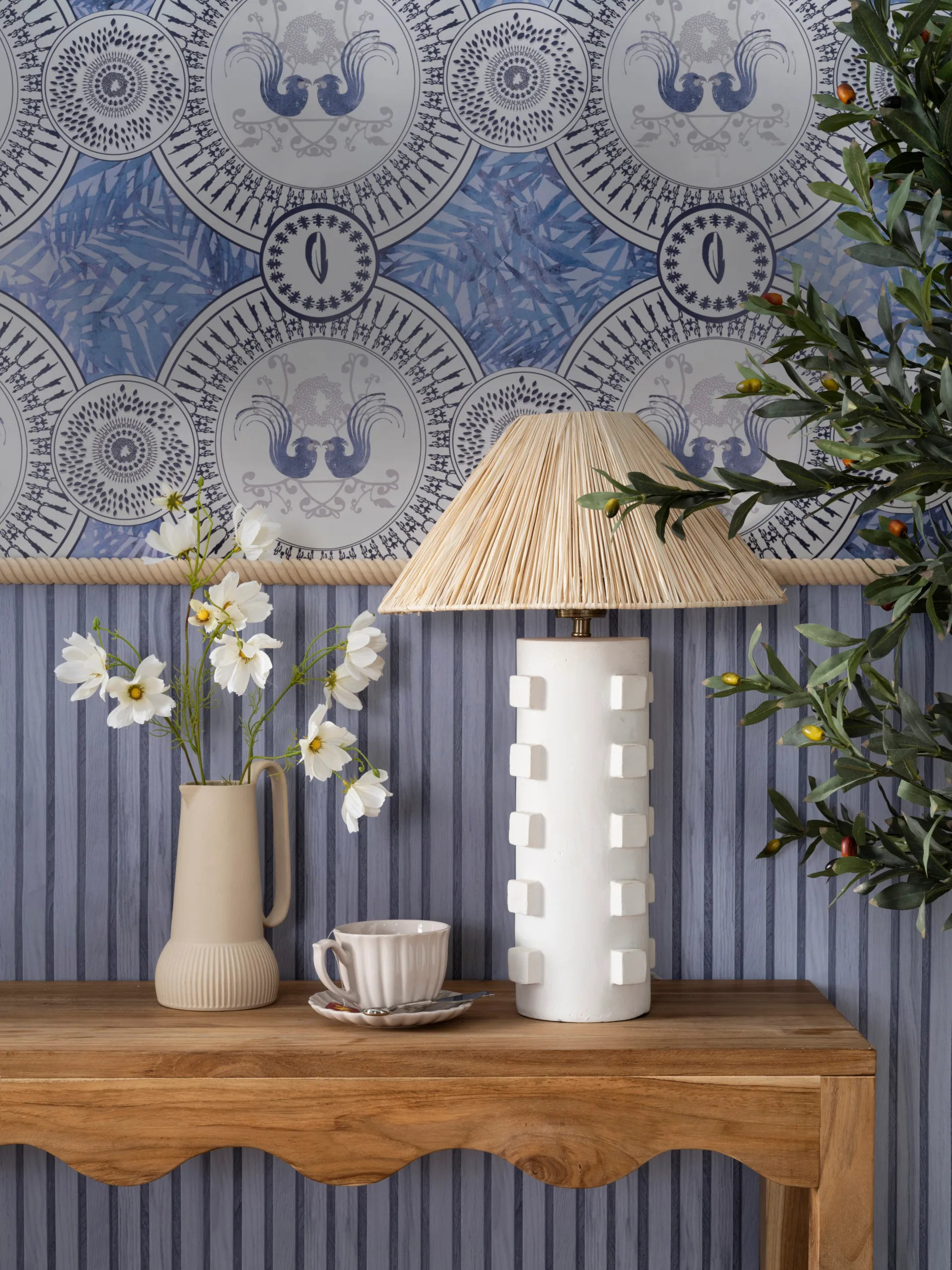 A timber console with a white lamp and a jug holding cosmos flowers.