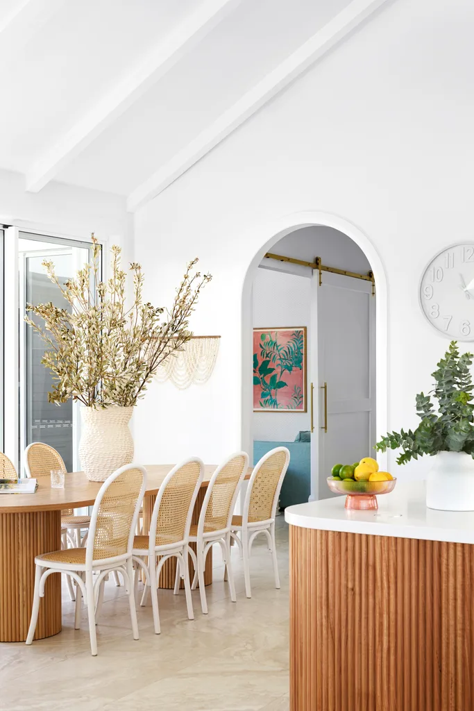 A coastal style dining area with a fluted timber table and white chairs.