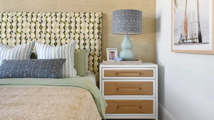 A coastal style kids bedroom with natural woven bedside drawers, a patterned upholstered bedhead and a surf artwork.