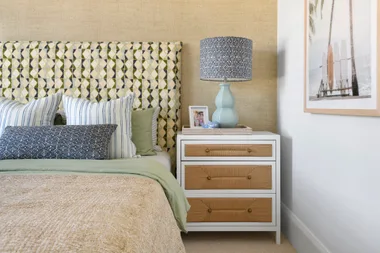 A coastal style kids bedroom with natural woven bedside drawers, a patterned upholstered bedhead and a surf artwork.