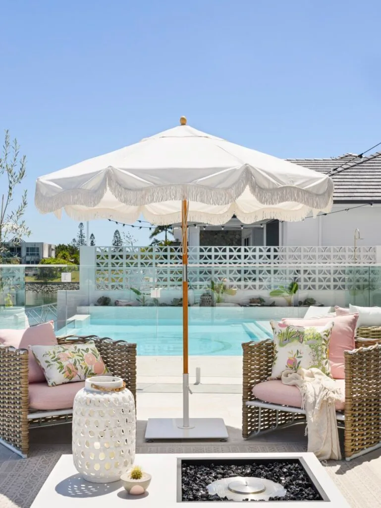 Outdoor pool landscaping ideas abound with wicker style armchairs and an umbrella.