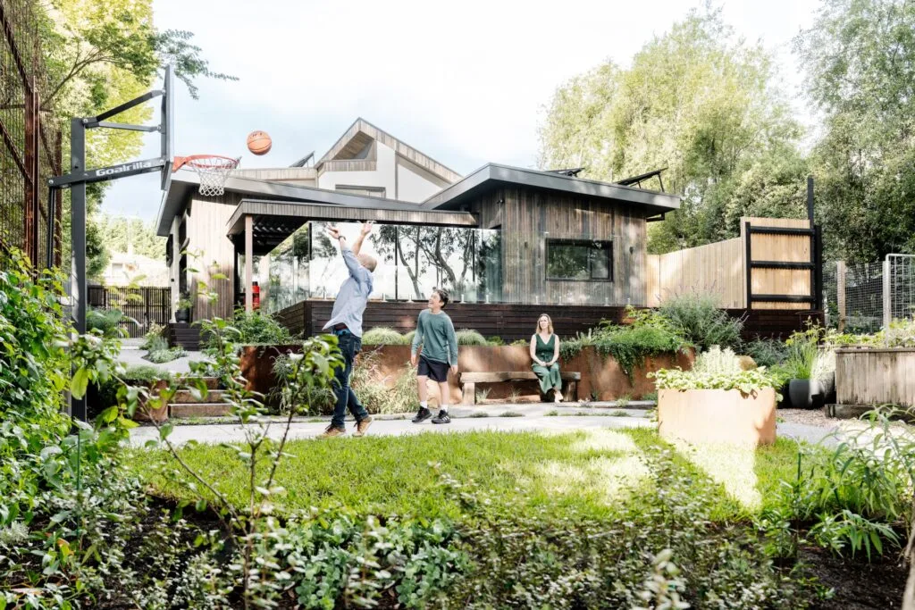 The family on the basketball court in the backyard by the home's rear facade.