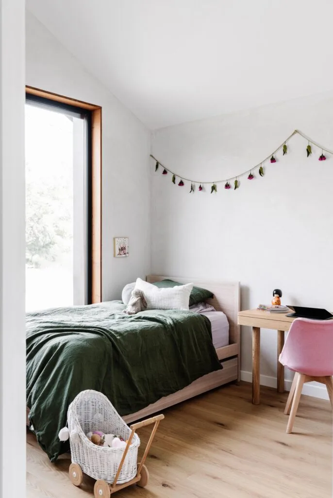 The children's bedroom with oak flooring and green linen on the bed.