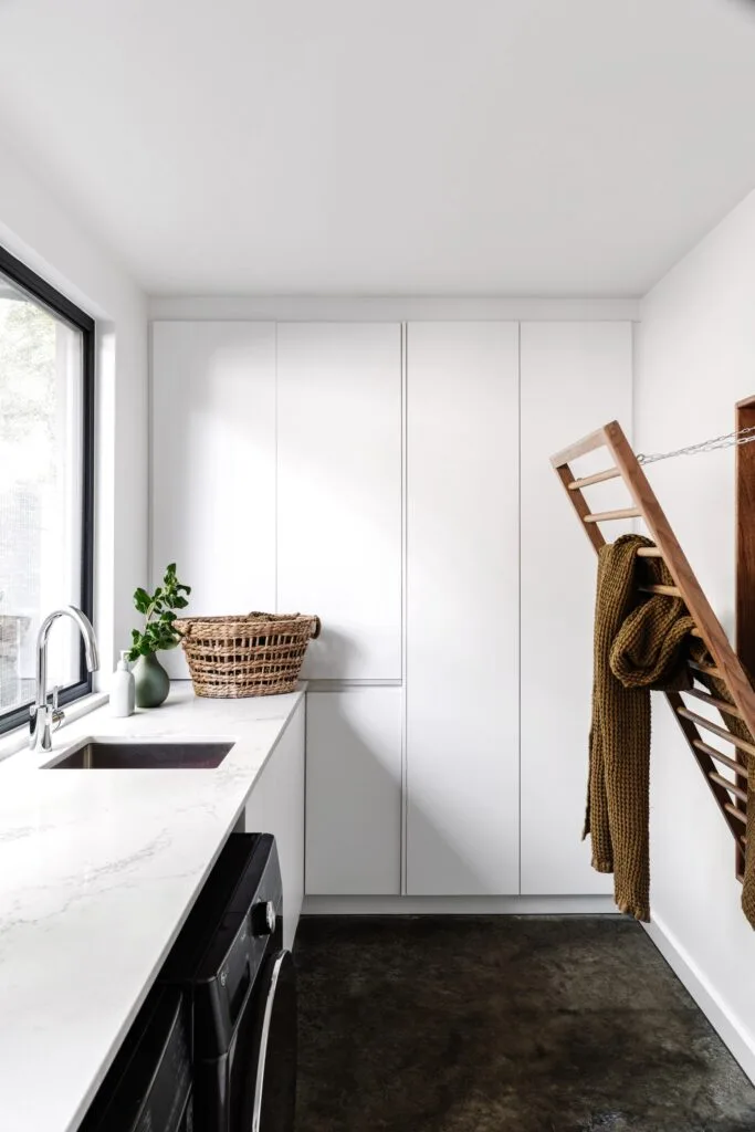 A white minimalist laundry with a timber drying rack.