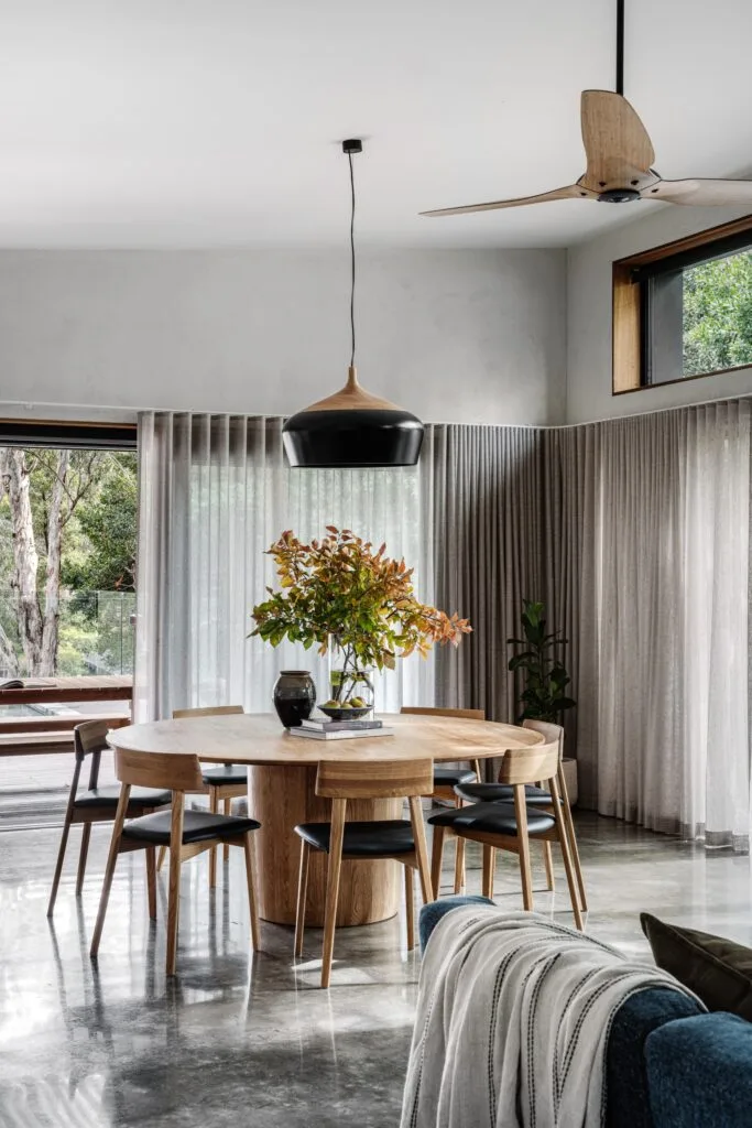 A minimalist dining room with a round timber table and a black light pendant.