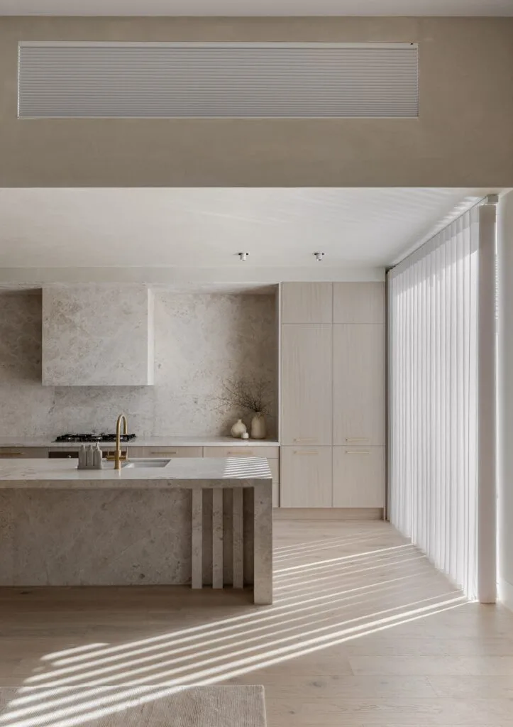 Minimalist stone kitchen with island, timber cupboards and clerestory window.