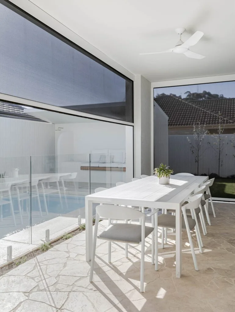 Outdoor alfresco area beside the pool with stone pavers and white table.