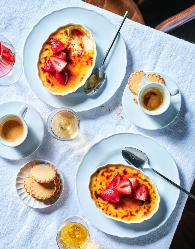 Two bowls of cr&egrave;me brulee topped with strawberries.