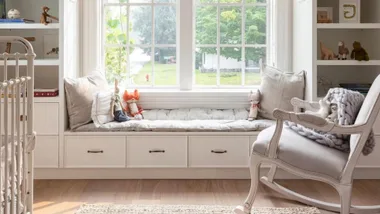 Neutral baby nursery with rocking chair, window seat and cot.