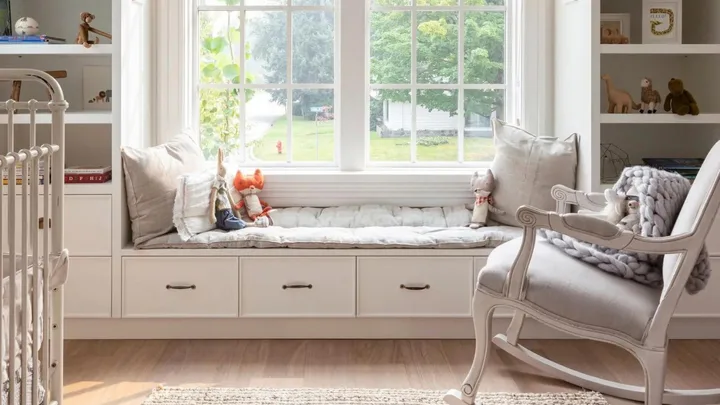 Neutral baby nursery with rocking chair, window seat and cot.