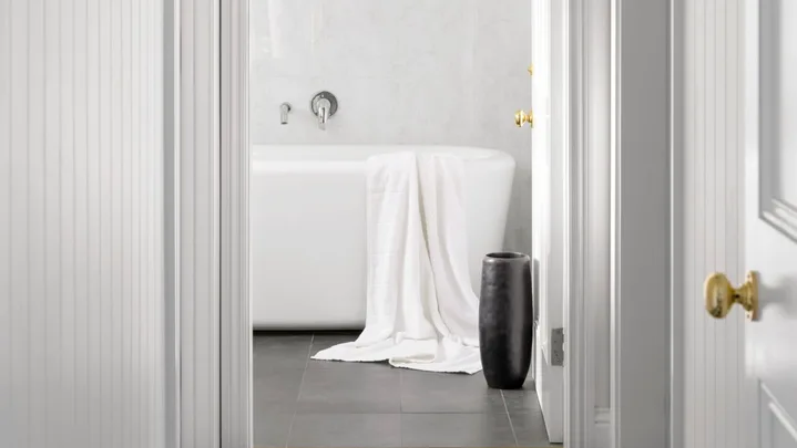 An all-white hallway with a checked floor leading to a bathroom.