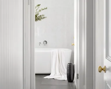 An all-white hallway with a checked floor leading to a bathroom.