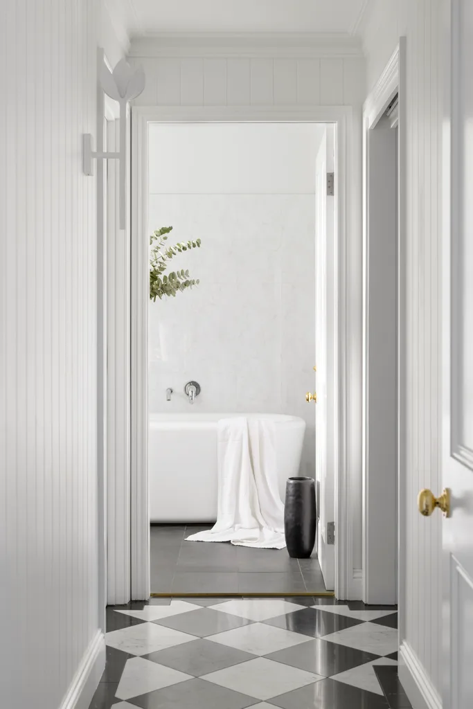 An all-white hallway with a checked floor leading to a bathroom.