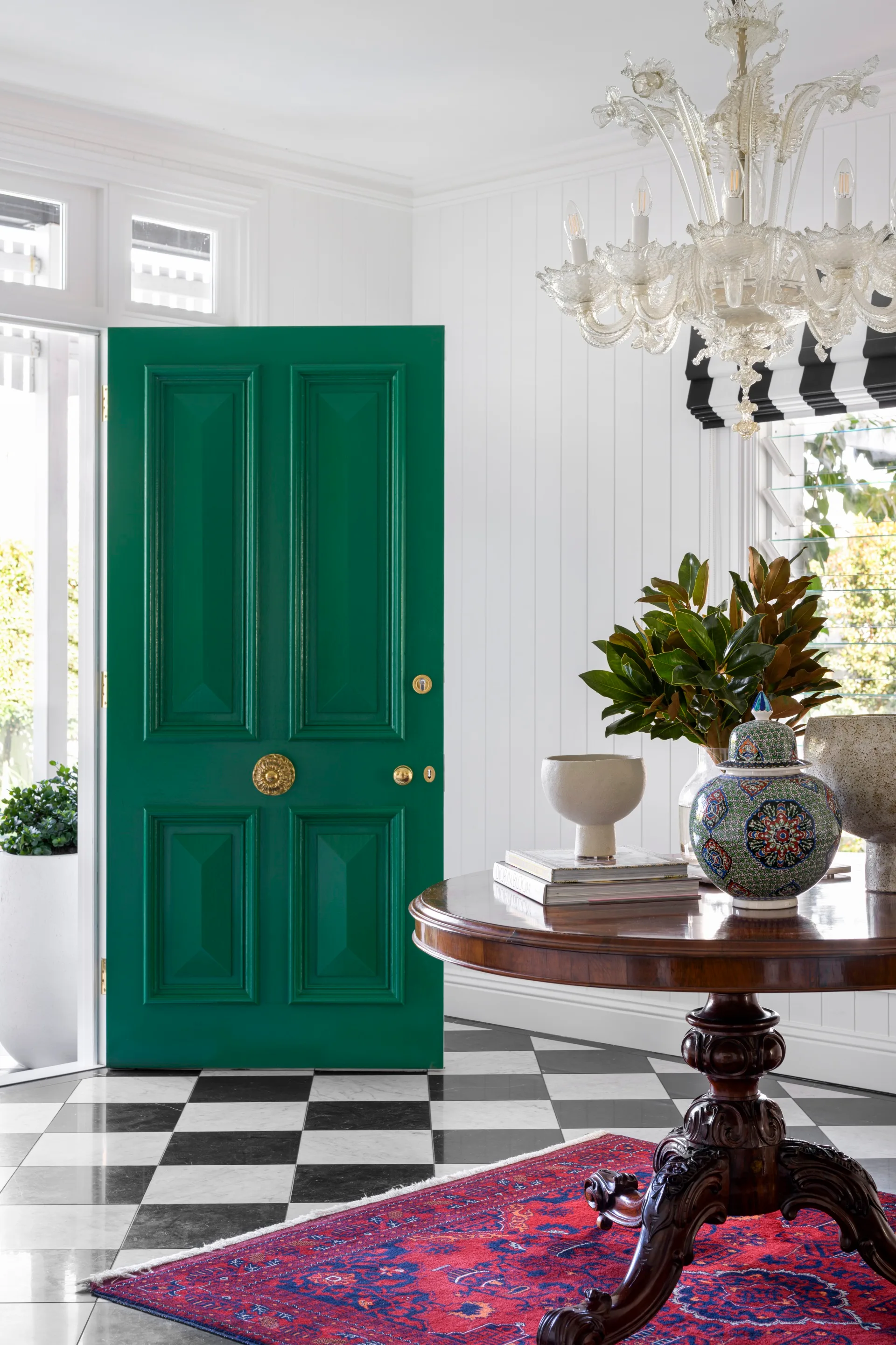 A foyer with a checked floor, green door and a vintage chandelier.