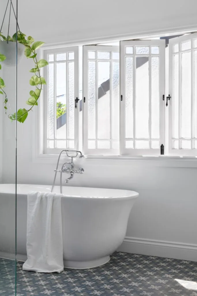 A white bathroom with casement windows and a free-standing porcelain bathtub.