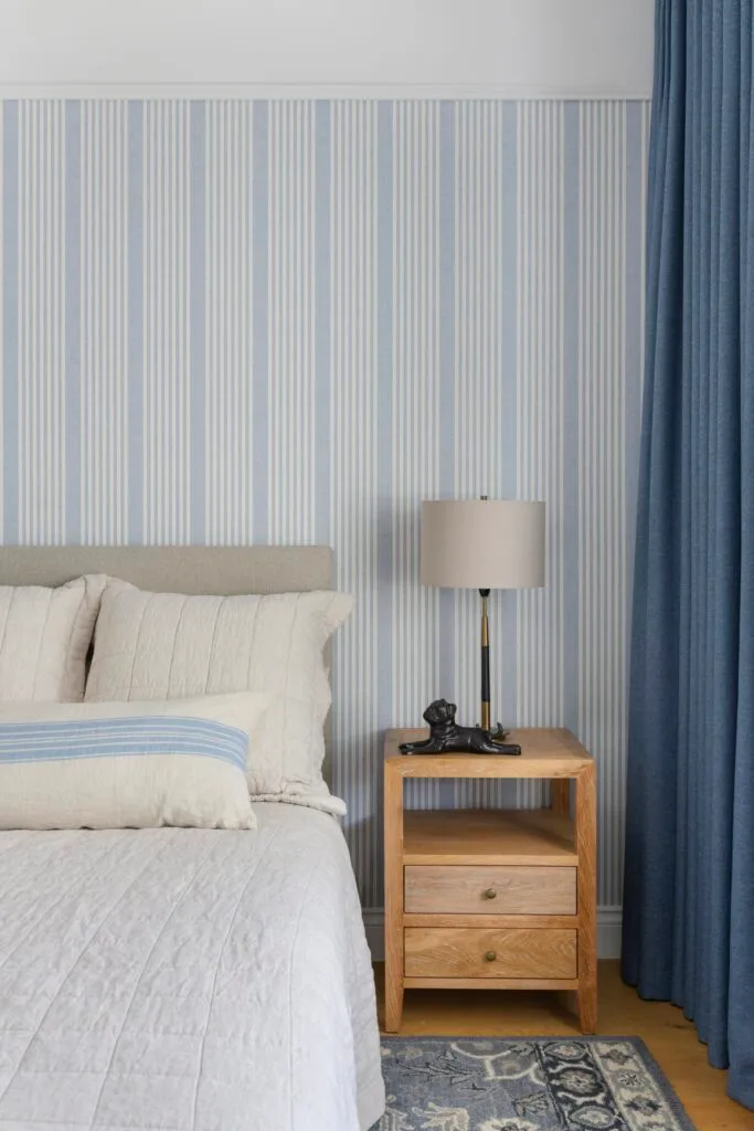 A children's bedroom with blue striped wallpaper and grey bed.