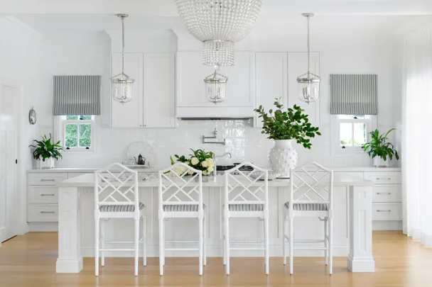 A classic white kitchen with a glass chandelier, island and striped window coverings.