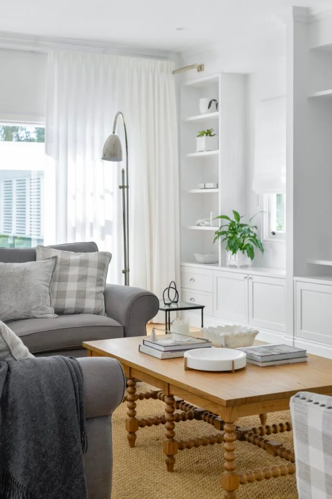 A white living room with a timber coffee table, grey sofas and open shelving.