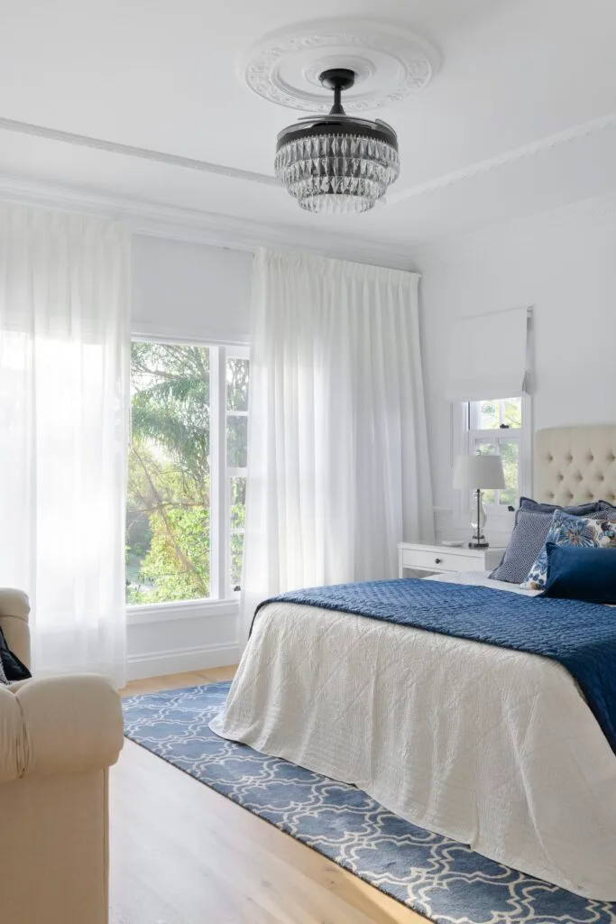 A white and blue main bedroom with an art deco style chandelier.