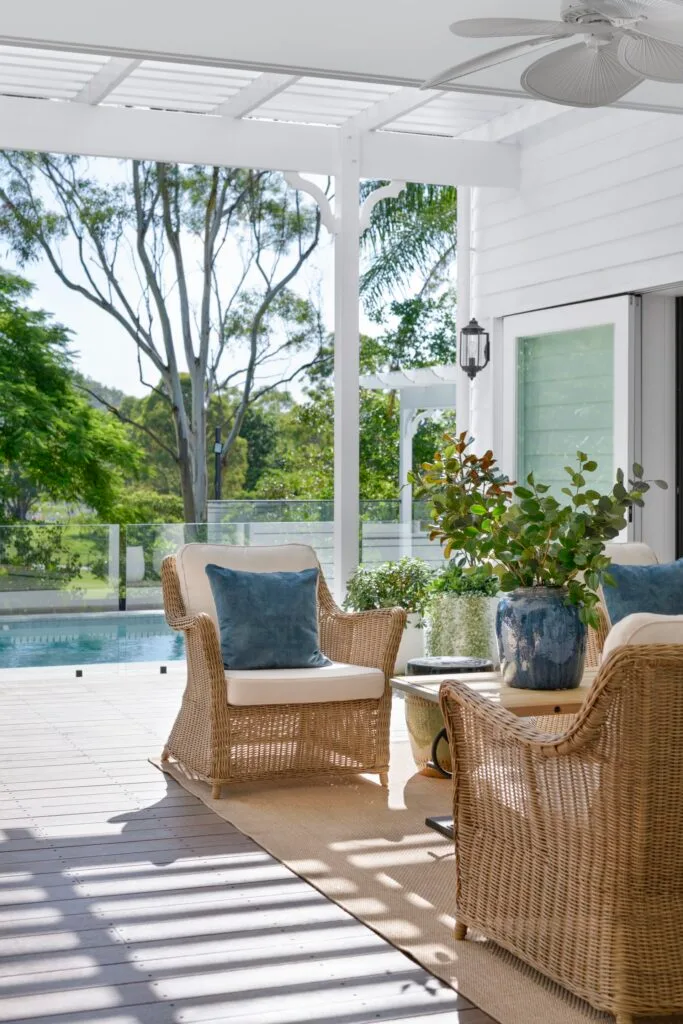 Wicker chairs in the white outdoor alfresco area by the pool.