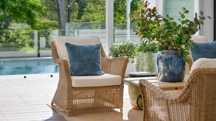 Wicker chairs in the white outdoor alfresco area by the pool.