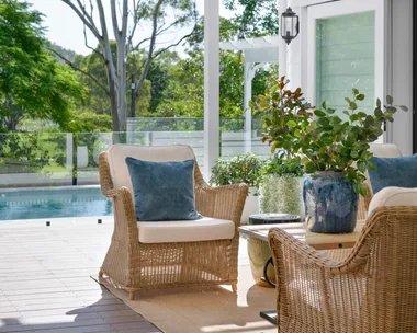 Wicker chairs in the white outdoor alfresco area by the pool.