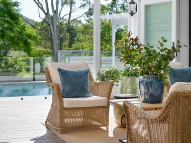 Wicker chairs in the white outdoor alfresco area by the pool.