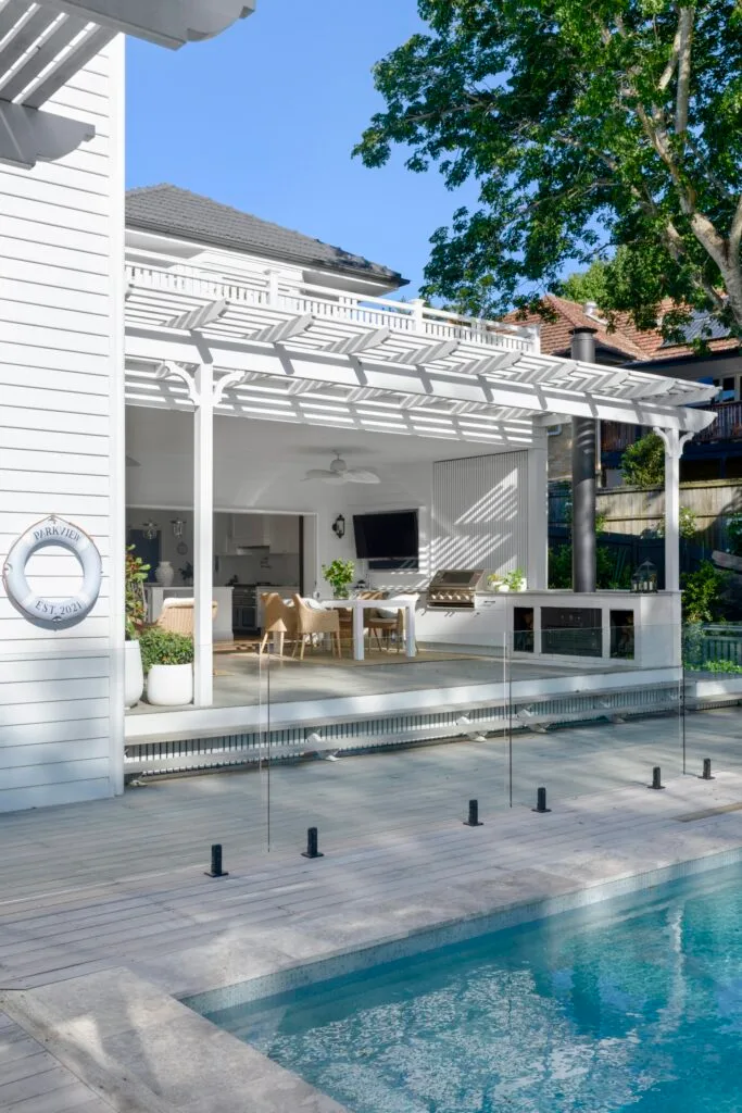 An white outdoor alfresco area by a glass enclosed pool.