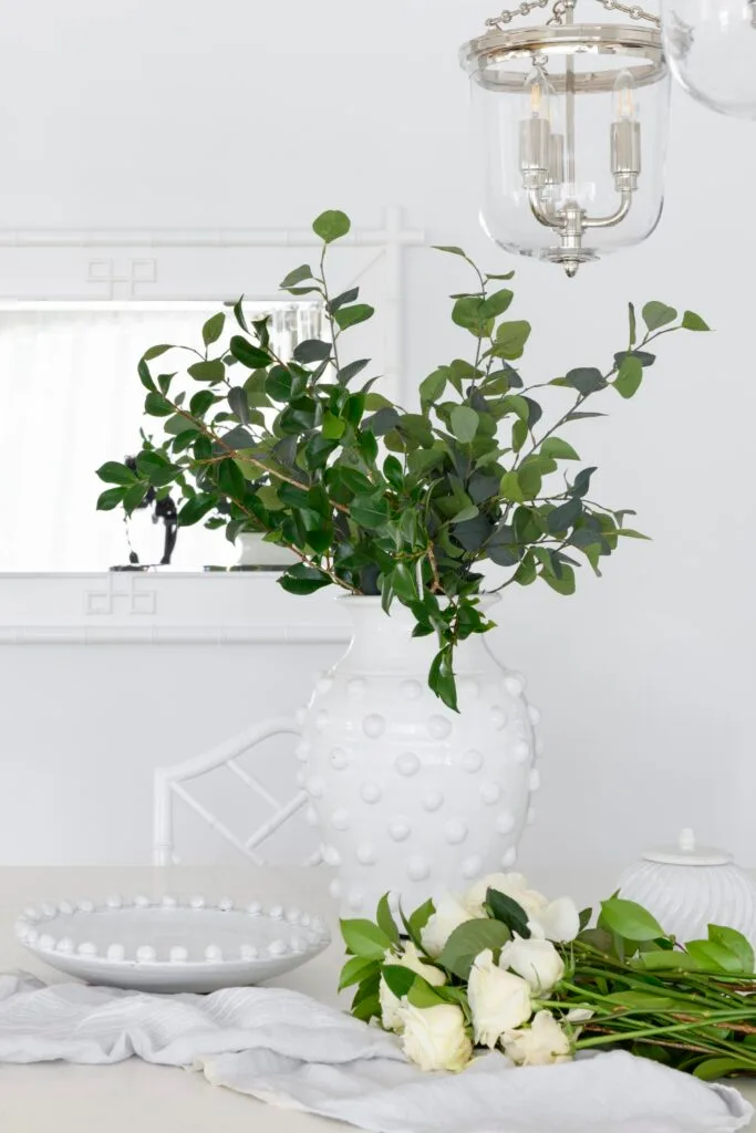 A white ceramic vase sitting on a dining table beneath a antique-style chandelier.