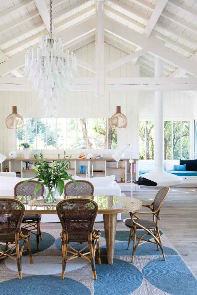 A white coastal living and dining room with a vintage dining table and a Murano chandelier.