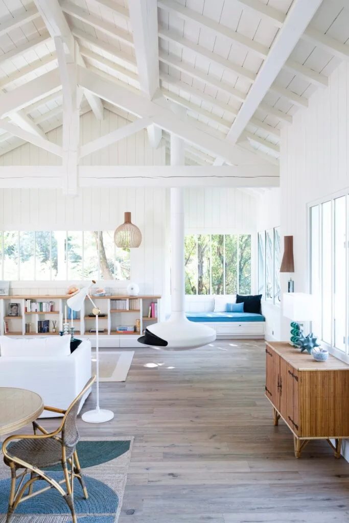 A coastal white living and dining room with a round suspended fireplace.