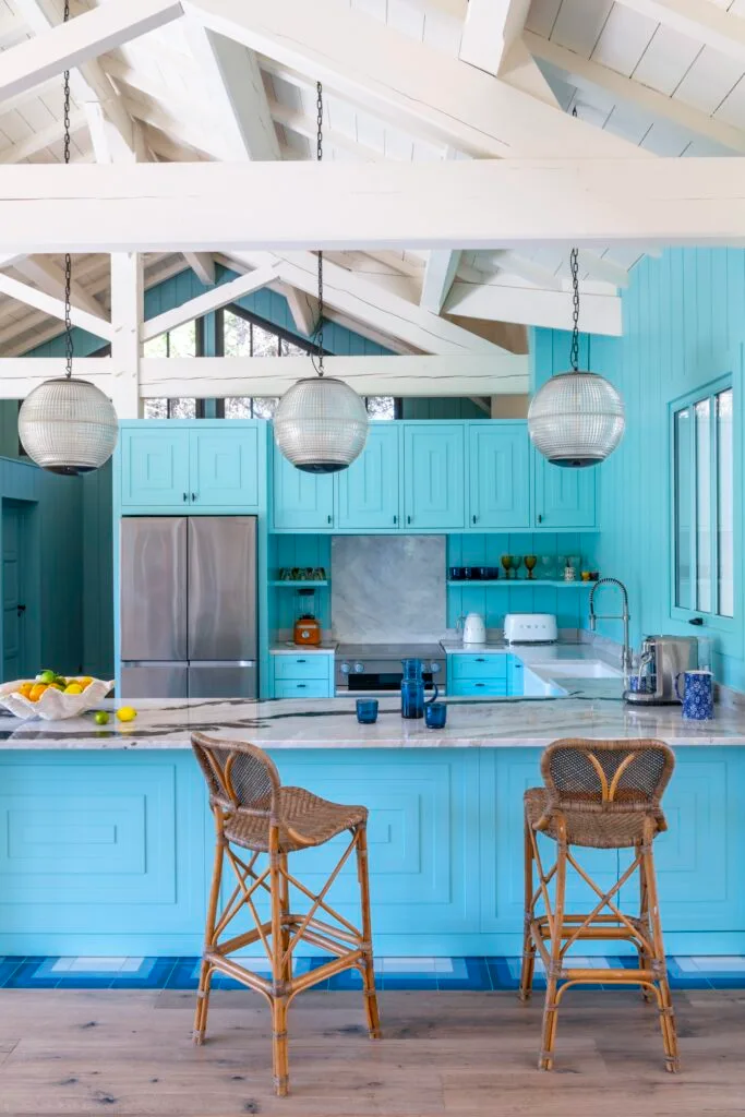 A coastal style kitchen with blue panelling, wicker stools and glass globe pendants.