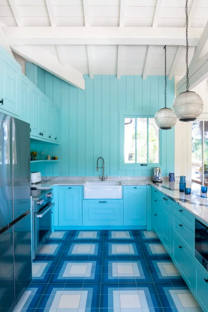 A coastal kitchen with blue wall panels, a butler's sink and geometric floor tiles.