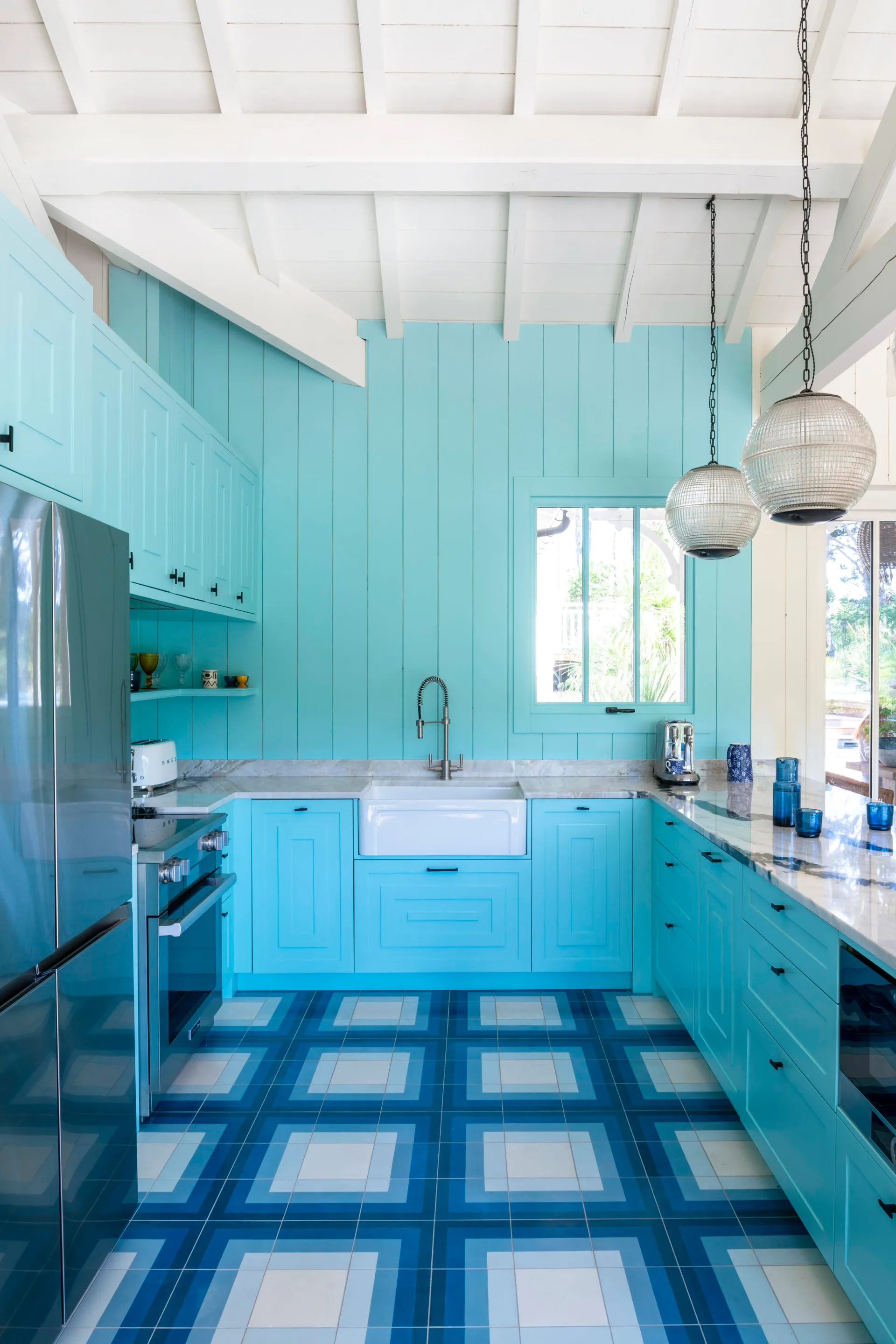 A coastal kitchen with blue wall panels, a butler's sink and geometric floor tiles.