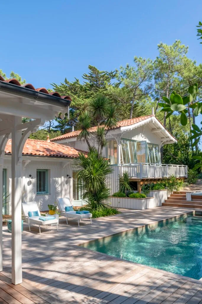 A pool and deck area with tropical plants by a white fenced balcony.