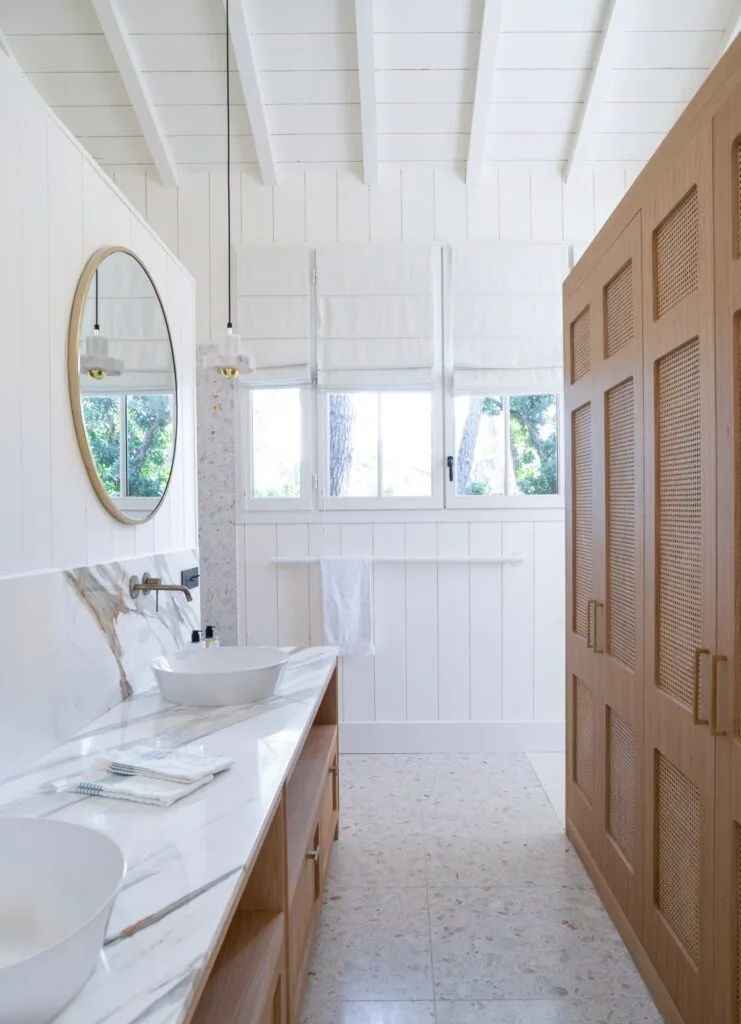 A white coastal bathroom with a marble vanity and timber wicker cabinets.