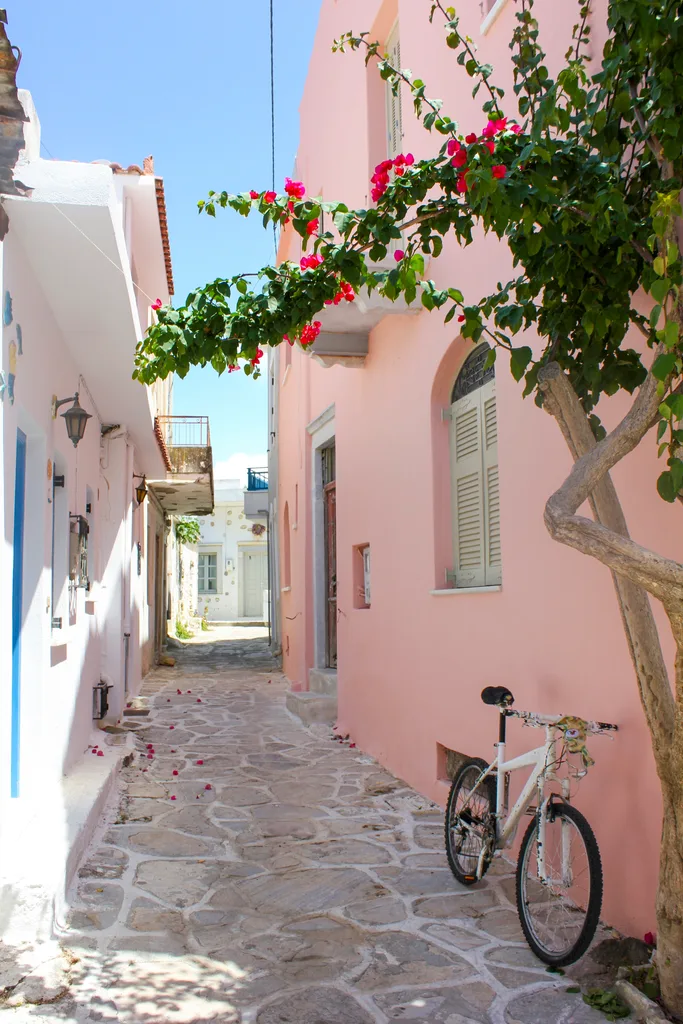 A stone alleyway between two pink and white buildings in Greece.