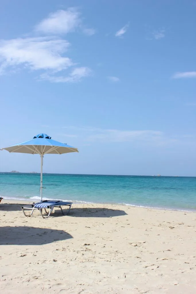 A beach with a blue umbrella and striped chair.