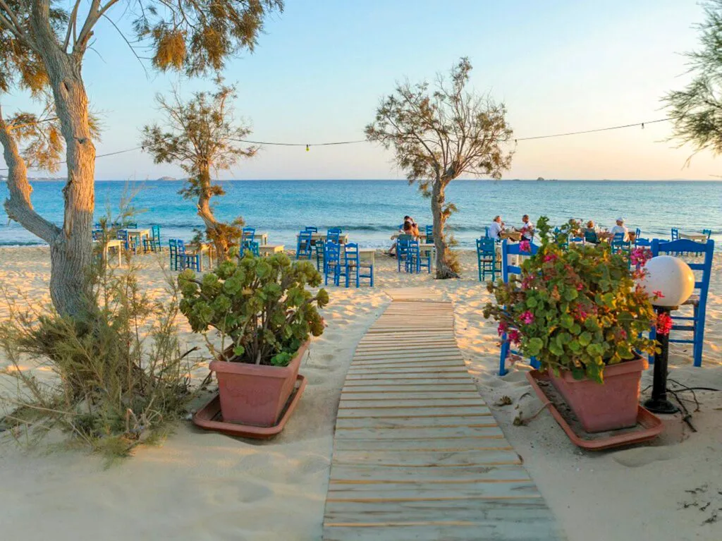 An outdoor beach restaurant with blue chairs and a wooden walkway.