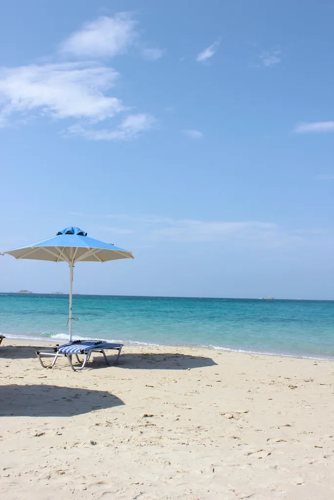 A beach with a blue umbrella and striped chair.