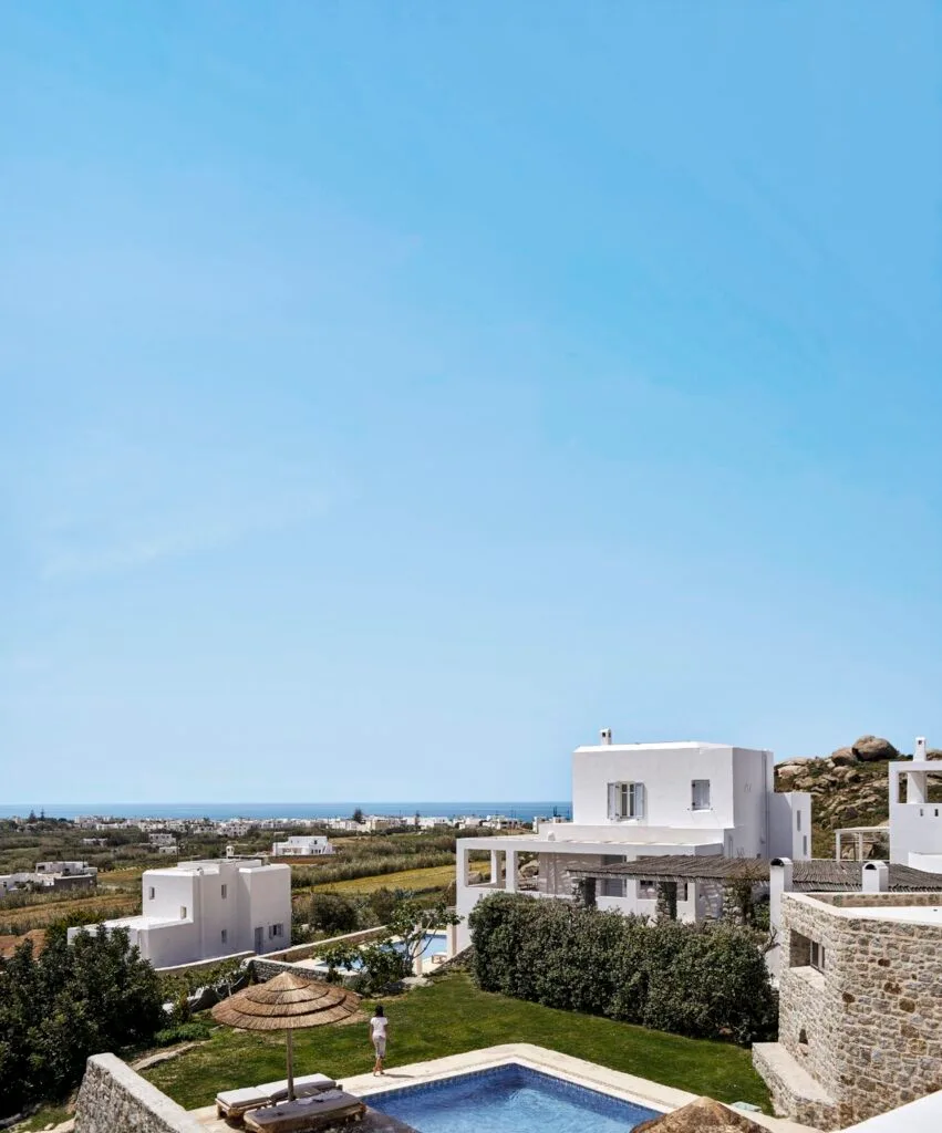 The exterior of white luxury villa and pool with the ocean in the distance.